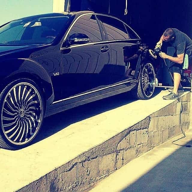 Detailer machine-polishing a black luxury car during paint correction in Chula Vista